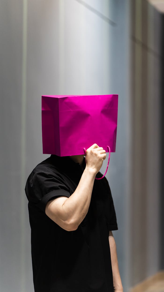 Man wearing a pink shopping bag on his head in a modern indoor setting.