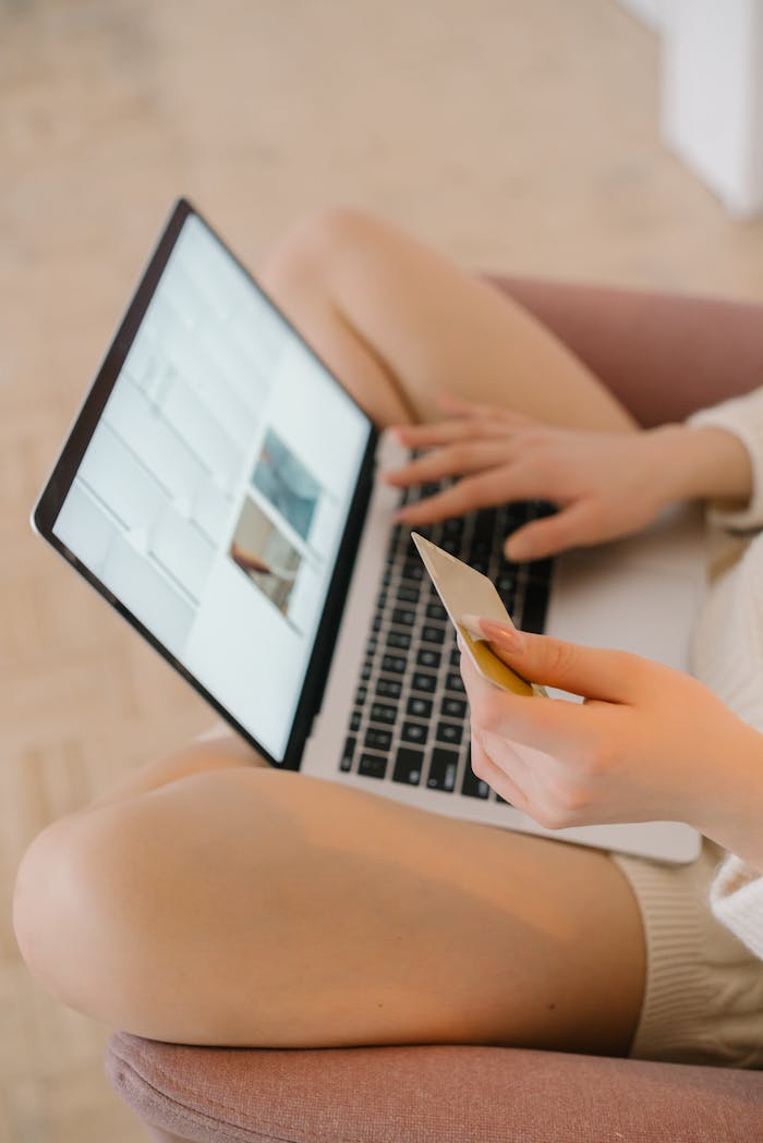 Woman holding a credit card while shopping online on a laptop from home.