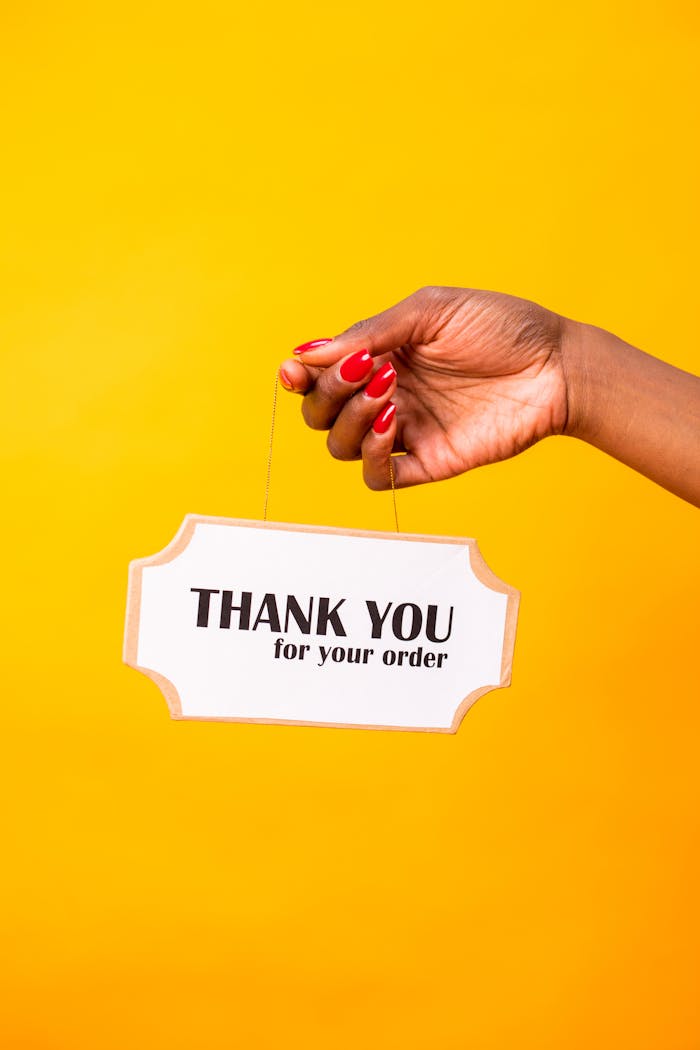 A hand holds a 'Thank You for Your Order' sign against a vibrant yellow background.